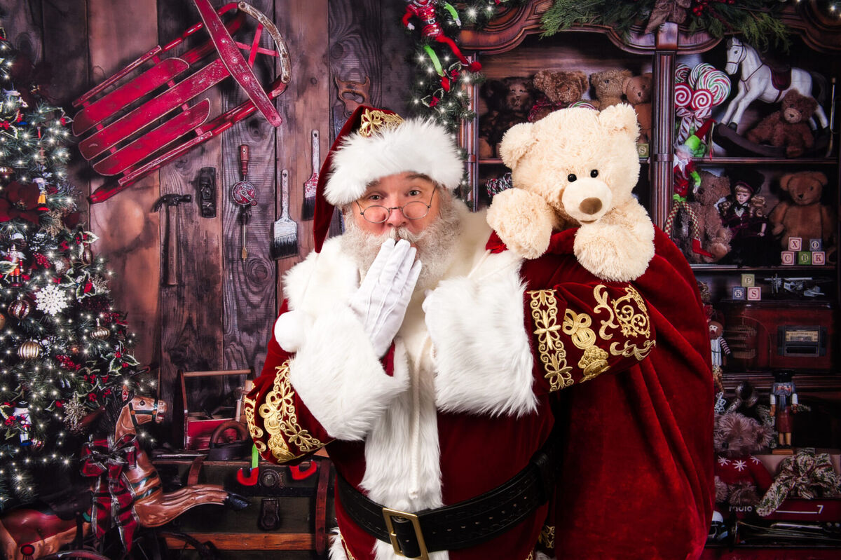 Santa Sarge blowing a kiss next to a teddy bear in a studio workshop set