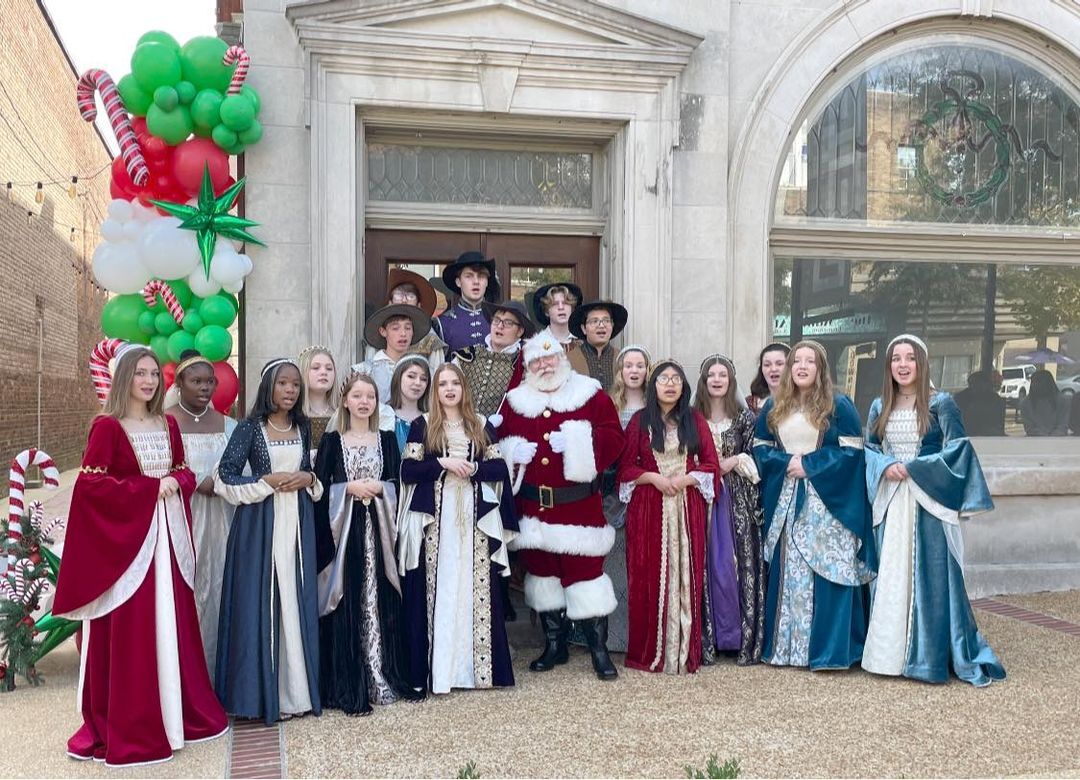 Santa Sarge with a costumed choir in front of a downtown building