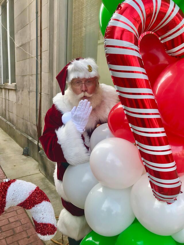 Santa Sarge with a little girl under a candy cane balloon arch