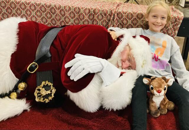 A girl giggling next to Santa Sarge pretending to sleep