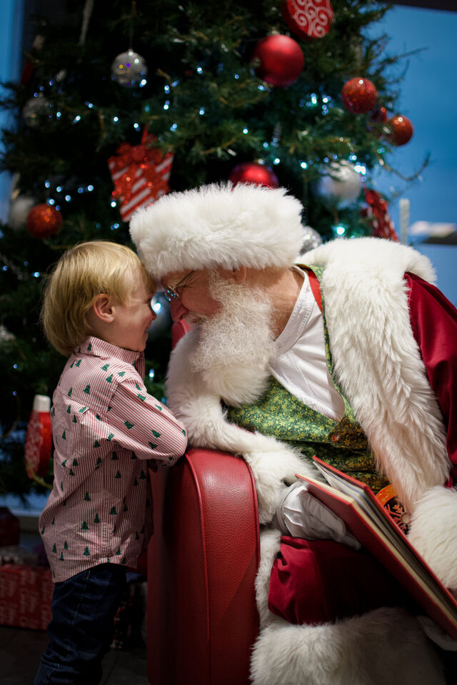 A child sitting with Santa Sarge by a Christmas tree