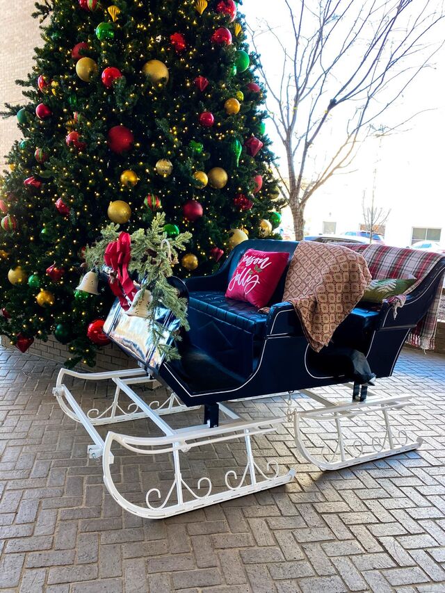 A red sleigh beside a Christmas tree ready for Santa