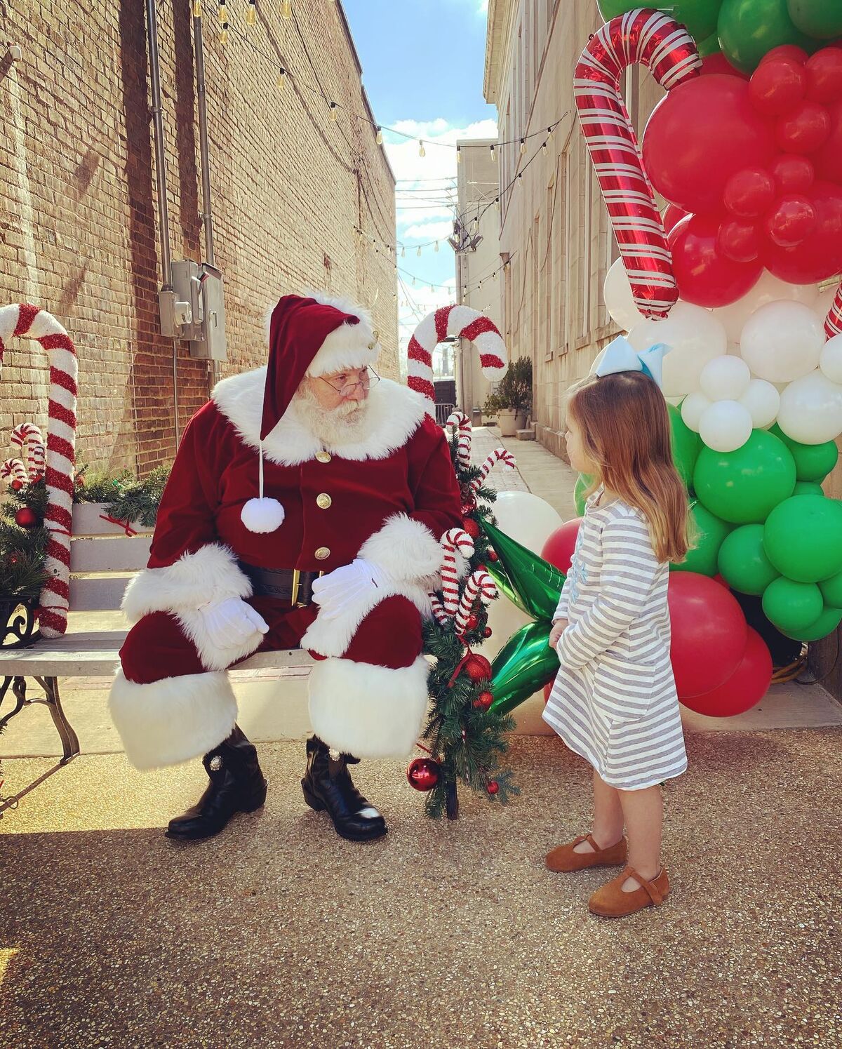 Santa Sarge greeting a little girl under a balloon arch