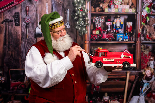 Santa Sarge in a green elf hat painting a toy fire truck