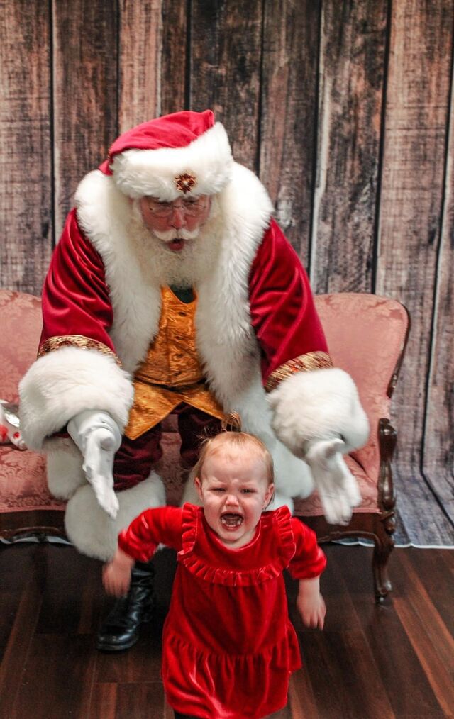 A baby in a red dress laughing in front of Santa Sarge